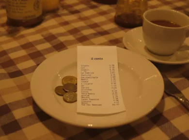 Napiwki we Włoszech - rachunek il conto z monetami euro na stoliku w trattorii