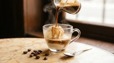 Filiżanka affogato - biała kulka gelato zalewana strumieniem gorącego espresso, unosząca się para, ziarna kawy i łyżeczka na kremowym marmurze