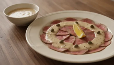 Cienkie plastry cielęciny na kremowym talerzu pod jasnym sosem tuńczykowym z kaparami i cytryną - vitello tonnato, piemoncki antipasto