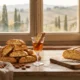 Cantuccini z całymi migdałami ułożone na drewnianym stole obok kieliszka vin santo, w tle przez okno toskańskie wzgórza z cyprysami